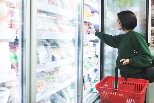A supermarket shopper opens a freezer to pull out some frozen food